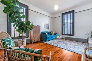 Een woonkamer met een blauwe bank, een houten kast, een grote groene plant en een rieten stoel.