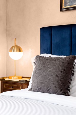 Een opgemaakt bed met een gekleurd kussen en een bedlampje op een houten nachtkastje.