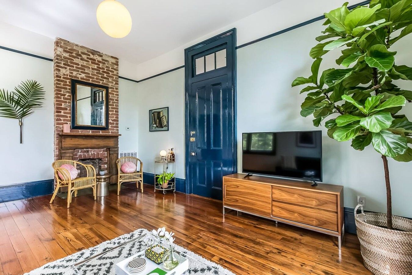 Ein Wohnzimmer mit Kamin aus Ziegelsteinen, einer blauen Tür, einem Fernseher und einer großen Grünpflanze.