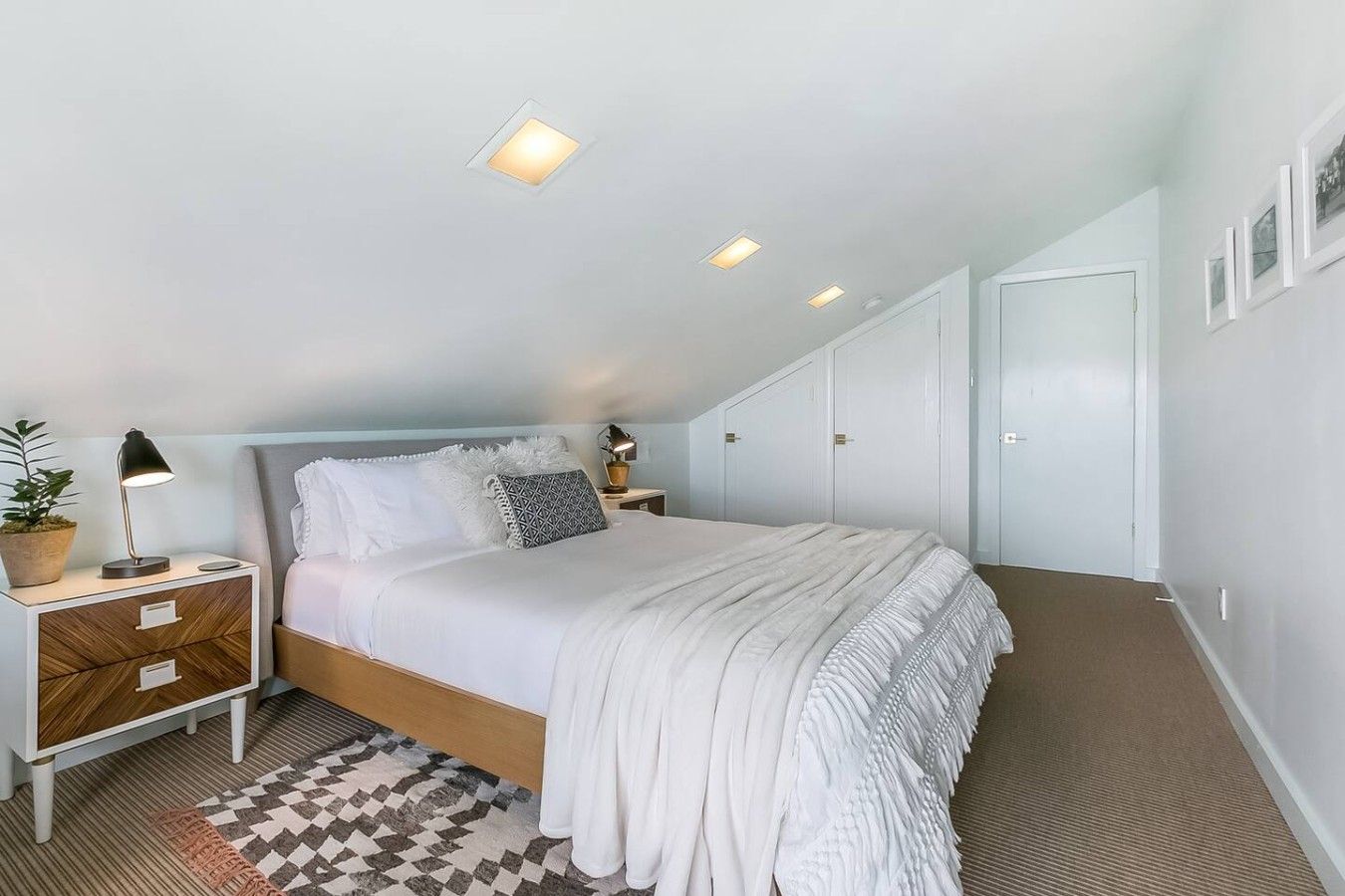 Une chambre à coucher avec un lit, des tables de chevet, une petite table, une plante en pot et un tapis à motifs.