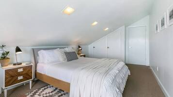 Une chambre à coucher avec un lit, des tables de chevet, une petite table, une plante en pot et un tapis à motifs.