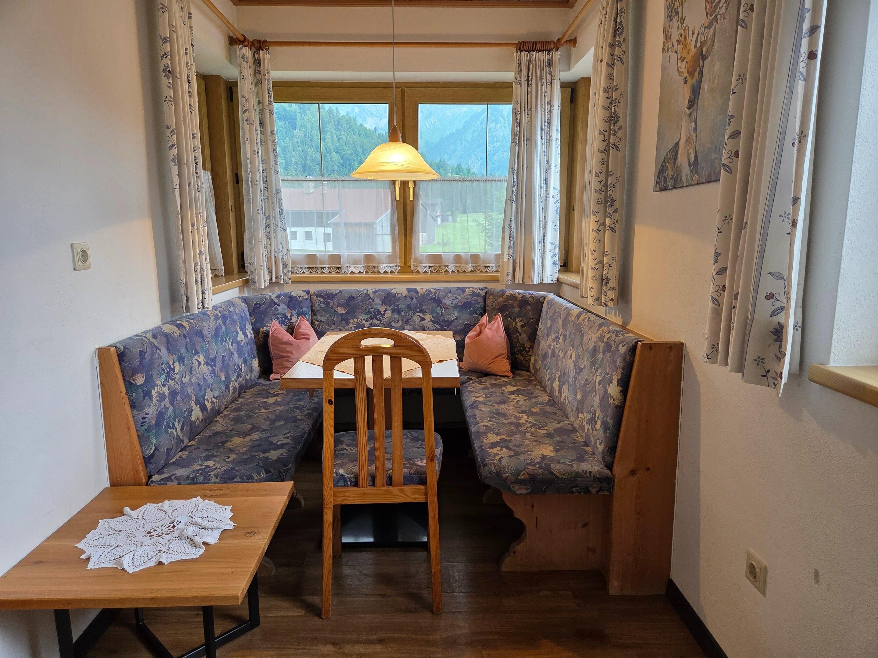 Eine Sitzecke mit Holztable und Bank, eine Hängelampe und Blick ins Freie.