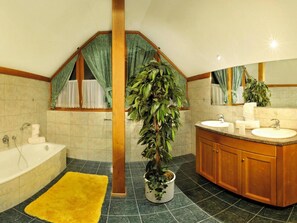 Ein Badezimmer mit einer Badewanne, einem Waschbecken und einem Spiegel. In der Mitte steht ein Blumentopf.