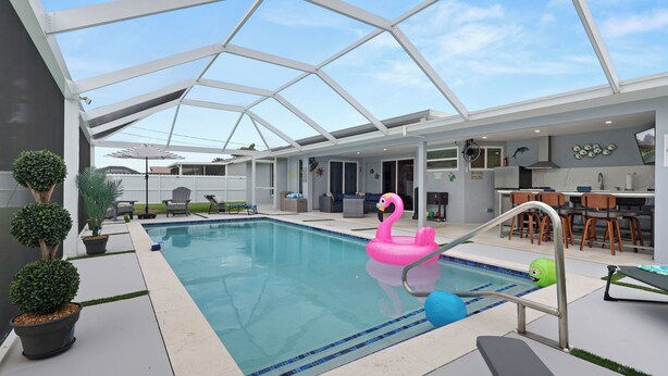 Et moderne poolområde indendørs med glastag, en lyserød flamingo flyder og et spiseområde med træstole.