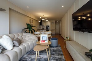 A modern living room with a sofa, a coffee table, and a dining area with chairs. - Vrbo Property (Miraflores)