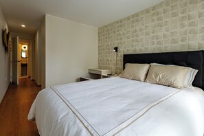 A hotel room with a large bed, a bedside table, a nightstand, and a wall-mounted lamp. - Vrbo Property (Miraflores)