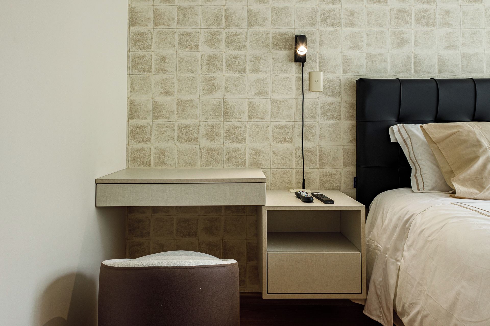 A neatly arranged hotel room with a bed, bedside table, lamp, and a small trash bin.