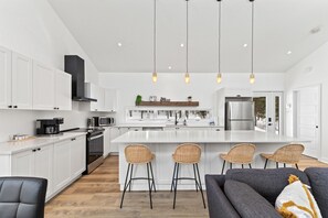 A modern kitchen with white cabinetry, a central island with bar stools, a stainless steel refrigerator, and a coffee machine. - Tremblant ski 8 min, Spa, Fireplace, Dog-Friendly (Lac-Supérieur)
