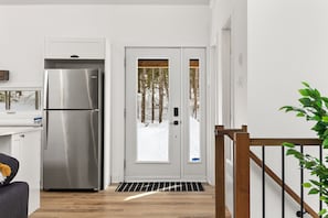A modern kitchen with a stainless steel refrigerator, a white door with a window, and a wooden staircase. - Tremblant ski 8 min, Spa, Fireplace, Dog-Friendly (Lac-Supérieur)
