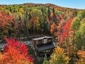A modern house with a flat roof, surrounded by a forest with autumn foliage. - Tremblant ski 8 min, Spa, Fireplace, Dog-Friendly (Lac-Supérieur)
