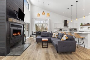 A modern living room with a fireplace, grey sofa, and dining area. - Tremblant ski 8 min, Spa, Fireplace, Dog-Friendly (Lac-Supérieur)