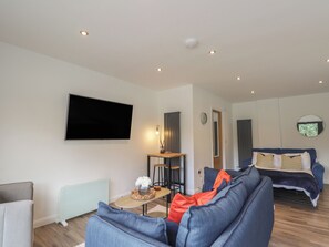 A modern living room with a flat-screen TV, a sofa, a coffee table, and a dining area with stools. - Broomfield Hideaway (Inverness)