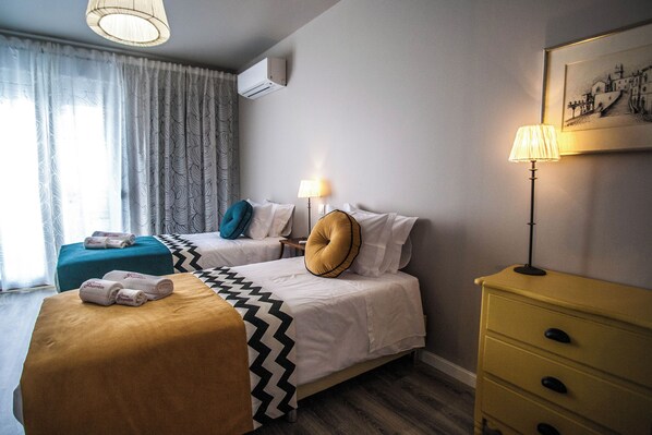 Una camera d'albergo con due letti, un comodino, una lampada, una cassettiera e una finestra con tende.