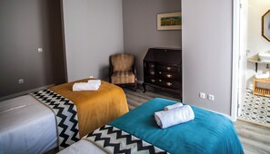 Una camera d'albergo con due letti, una sedia, un comò e un bagno visibile attraverso una porta aperta.