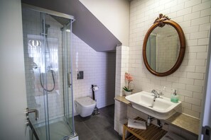 Un bagno con doccia vetrata, un water, un lavandino con specchio e una piccola pianta in vaso.