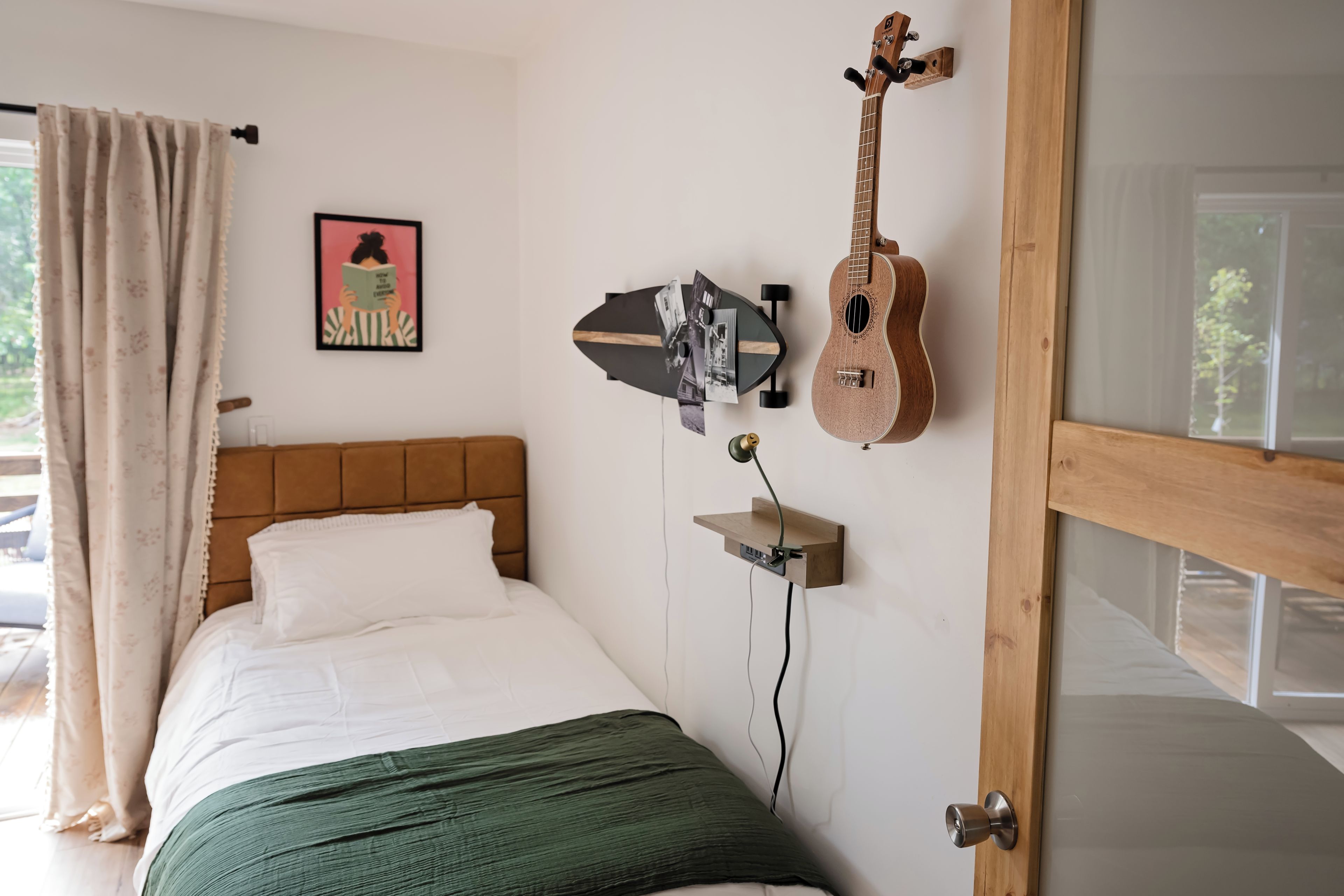 A bedroom with a bed, a guitar, a picture on the wall, and a window with curtains.