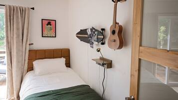 A bedroom with a bed, a guitar, a picture on the wall, and a window with curtains.
