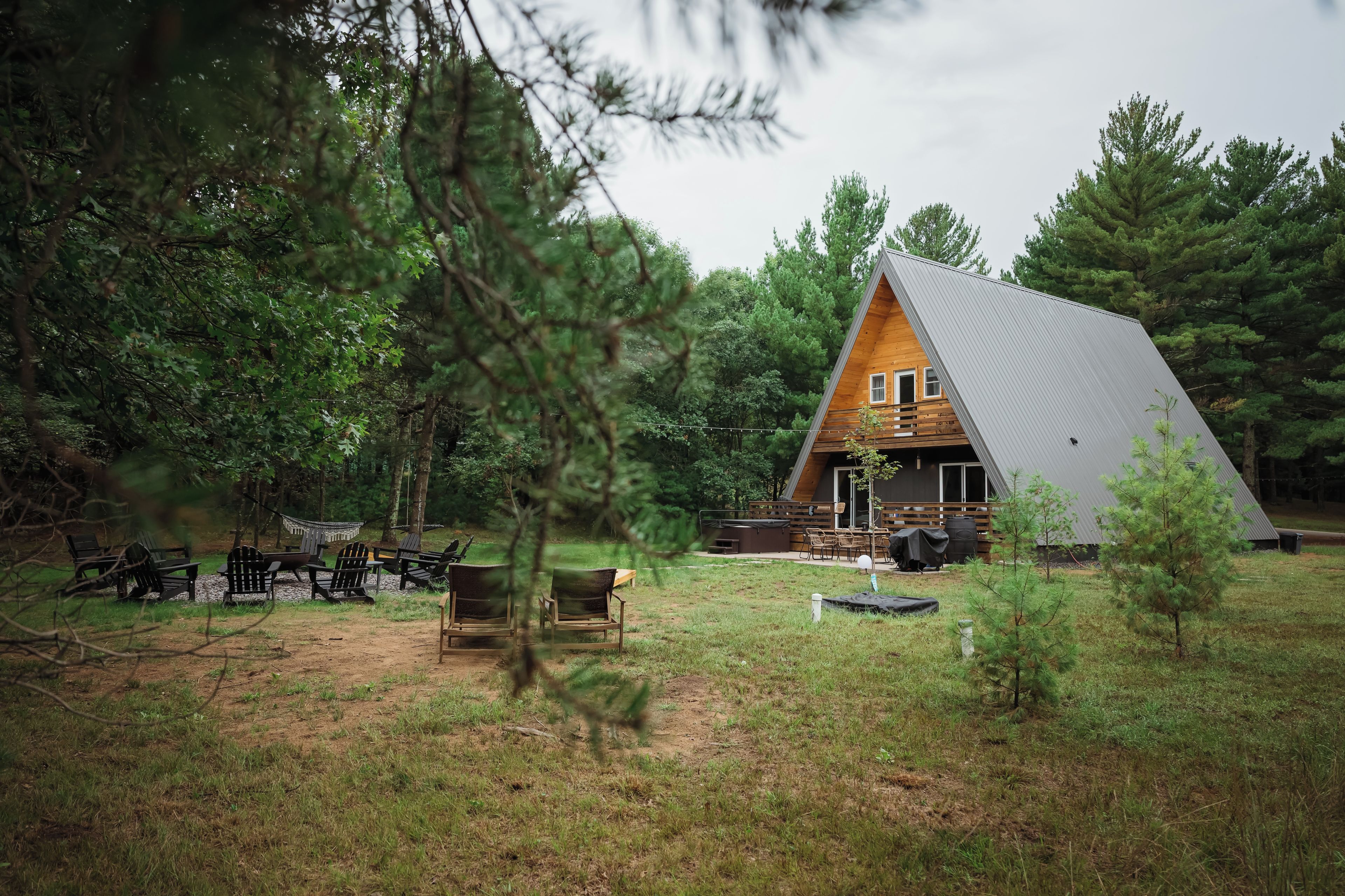 A cabin with a sloped roof, surrounded by trees and a grassy area with outdoor seating.