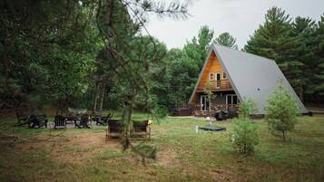 A cabin with a sloped roof, surrounded by trees and a grassy area with outdoor seating.