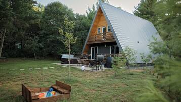 A modern A-frame house with a deck, outdoor furniture, and a sandbox.