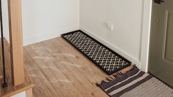 A hallway with a wooden floor, a black and white rug, a mirror, and a framed poster on the wall.