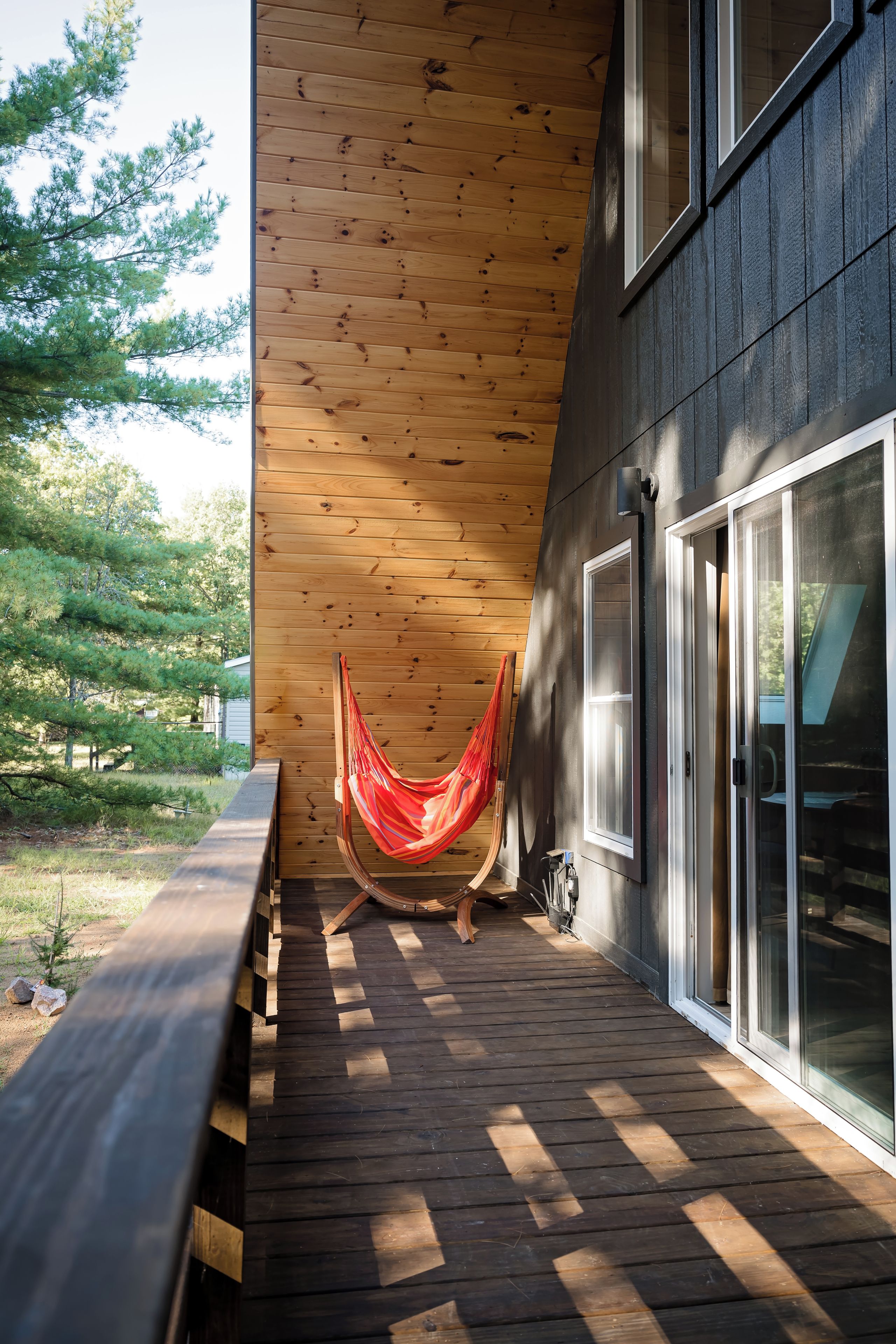 A wooden deck with a hammock, a bench, and a glass door leading to a covered area.