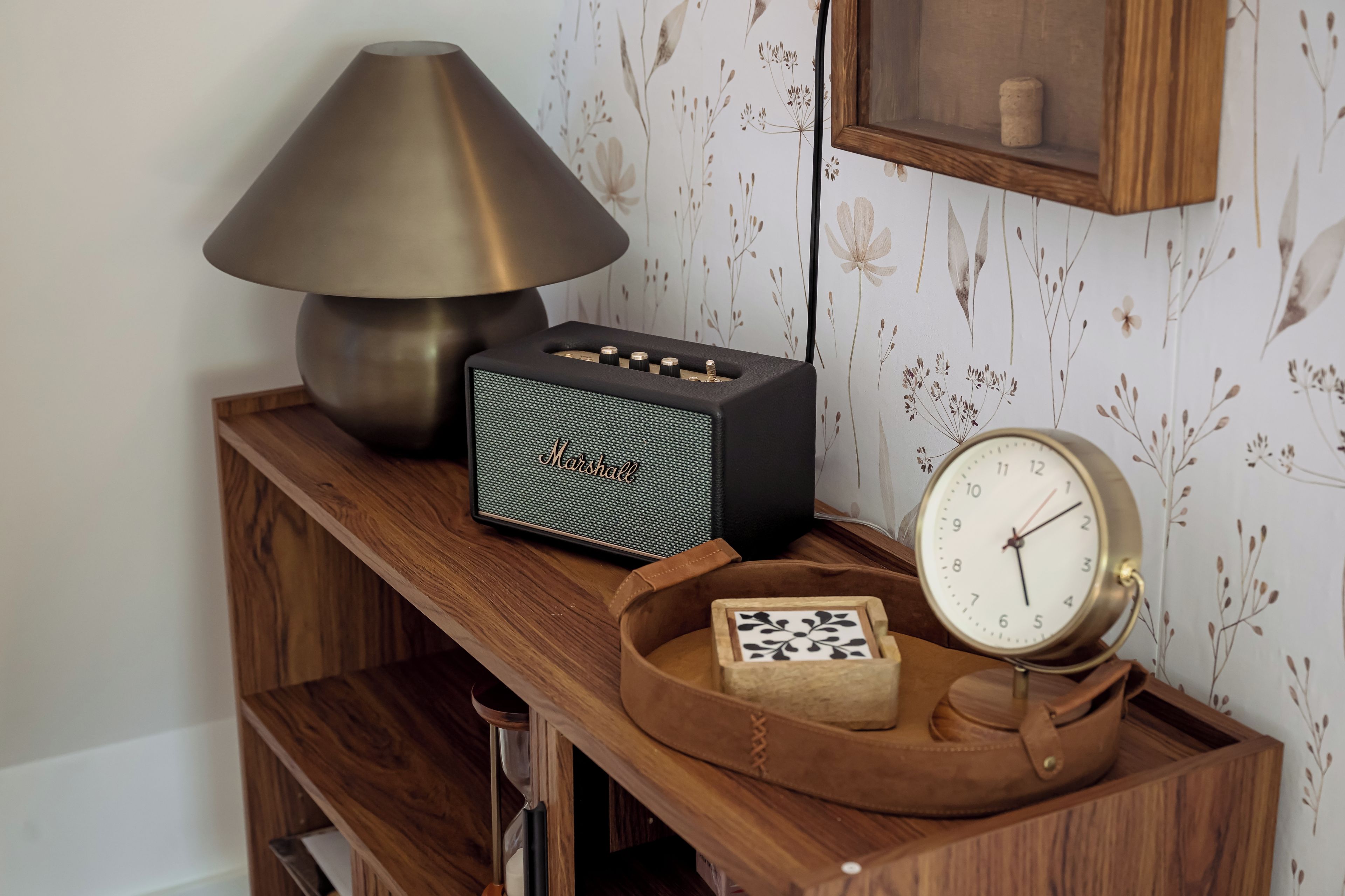 Una estantería de madera con una lámpara, un radio, un reloj y un bolso de cuero.