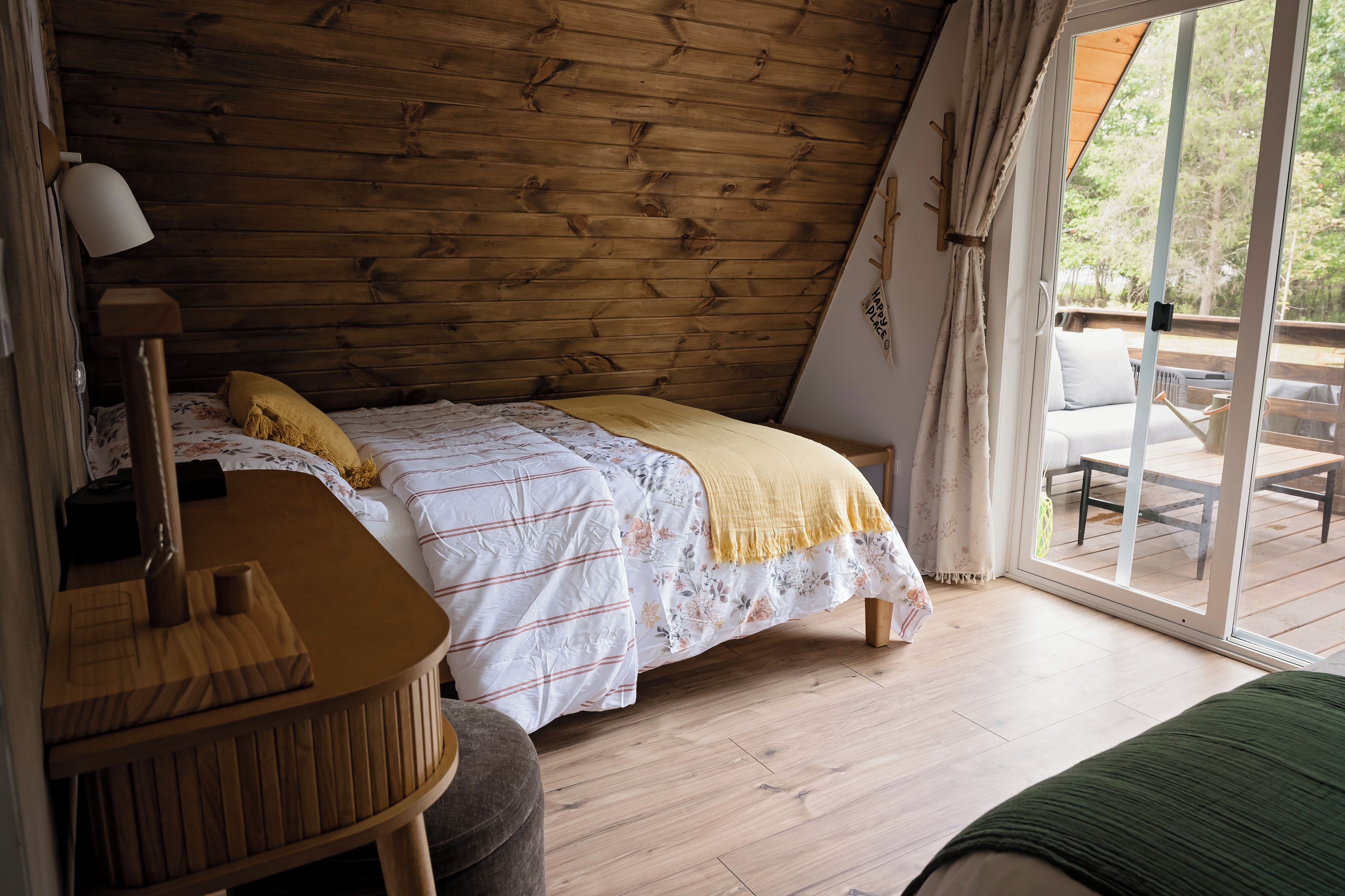 Un dormitorio con techo de madera, cama con ropa de cama floral, un escritorio y vista a una terraza exterior.