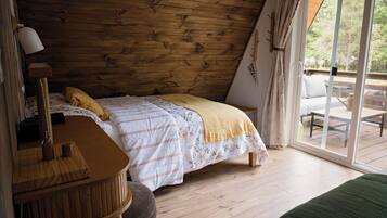 Un dormitorio con techo de madera, cama con ropa de cama floral, un escritorio y vista a una terraza exterior.