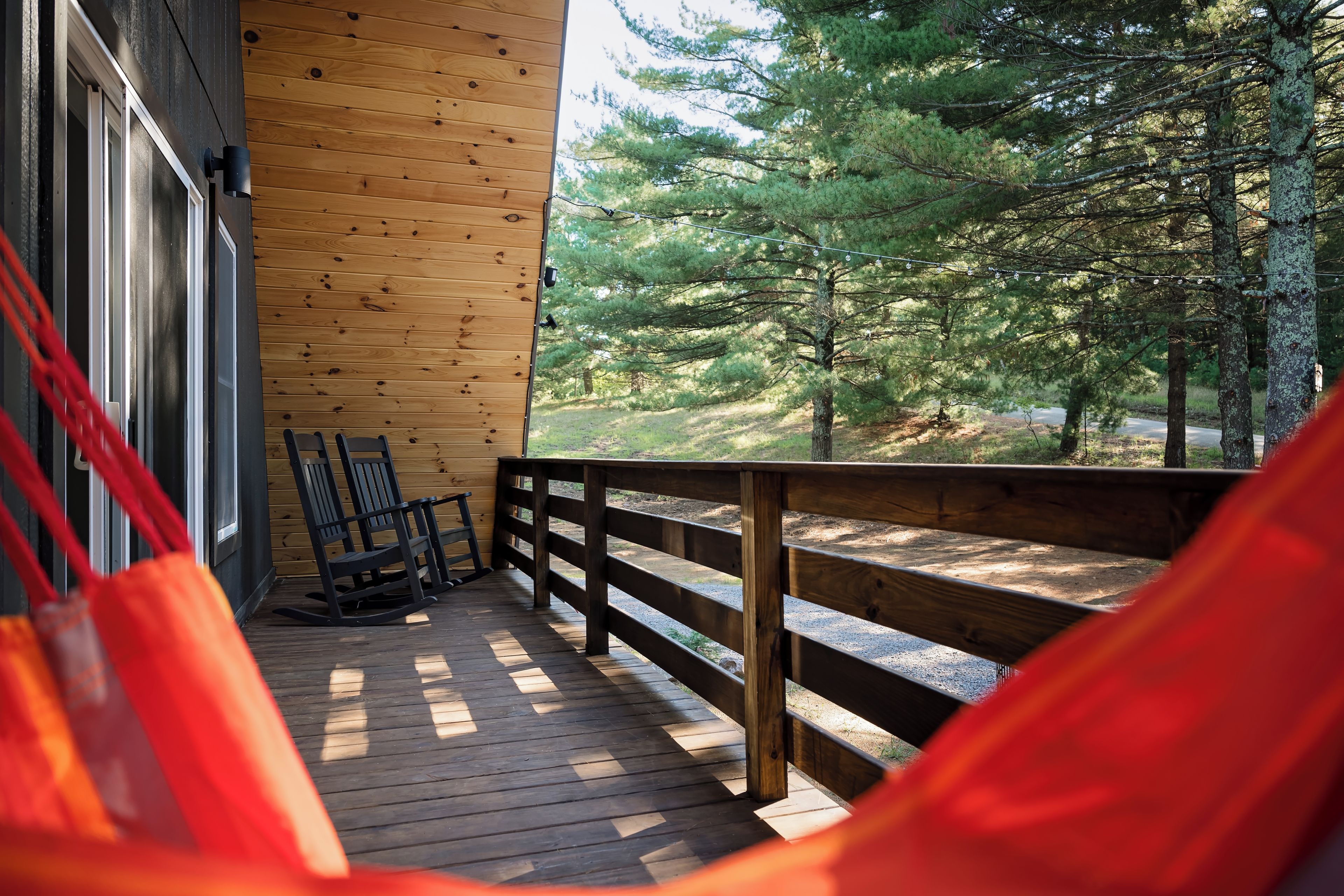 A wooden deck with a rocking chair and a hammock, overlooking a forested area.