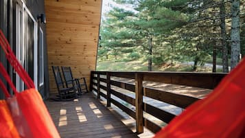 A wooden deck with a rocking chair and a hammock, overlooking a forested area.