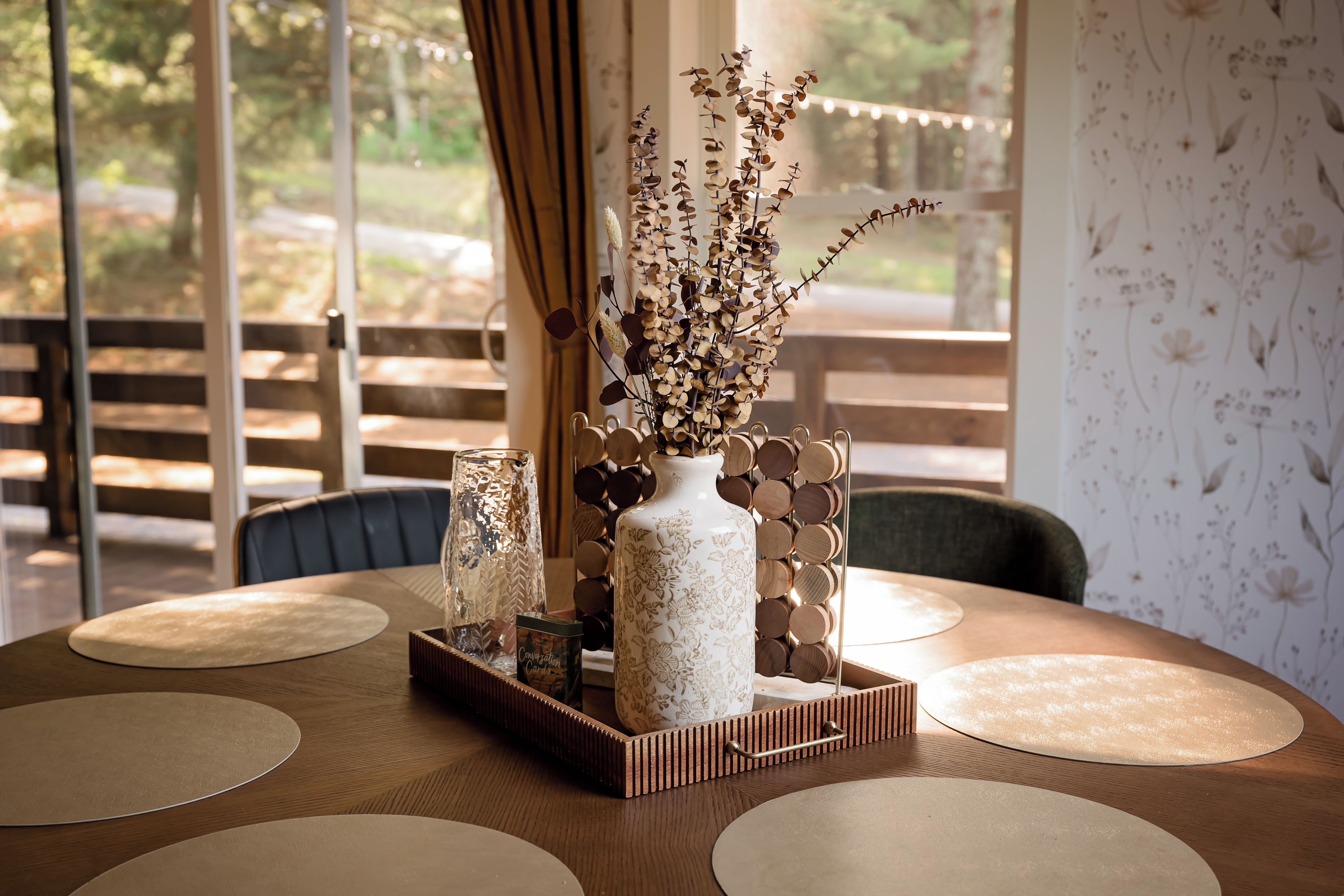 A round table with a vase of dried flowers, a glass vase, and a wooden tray.