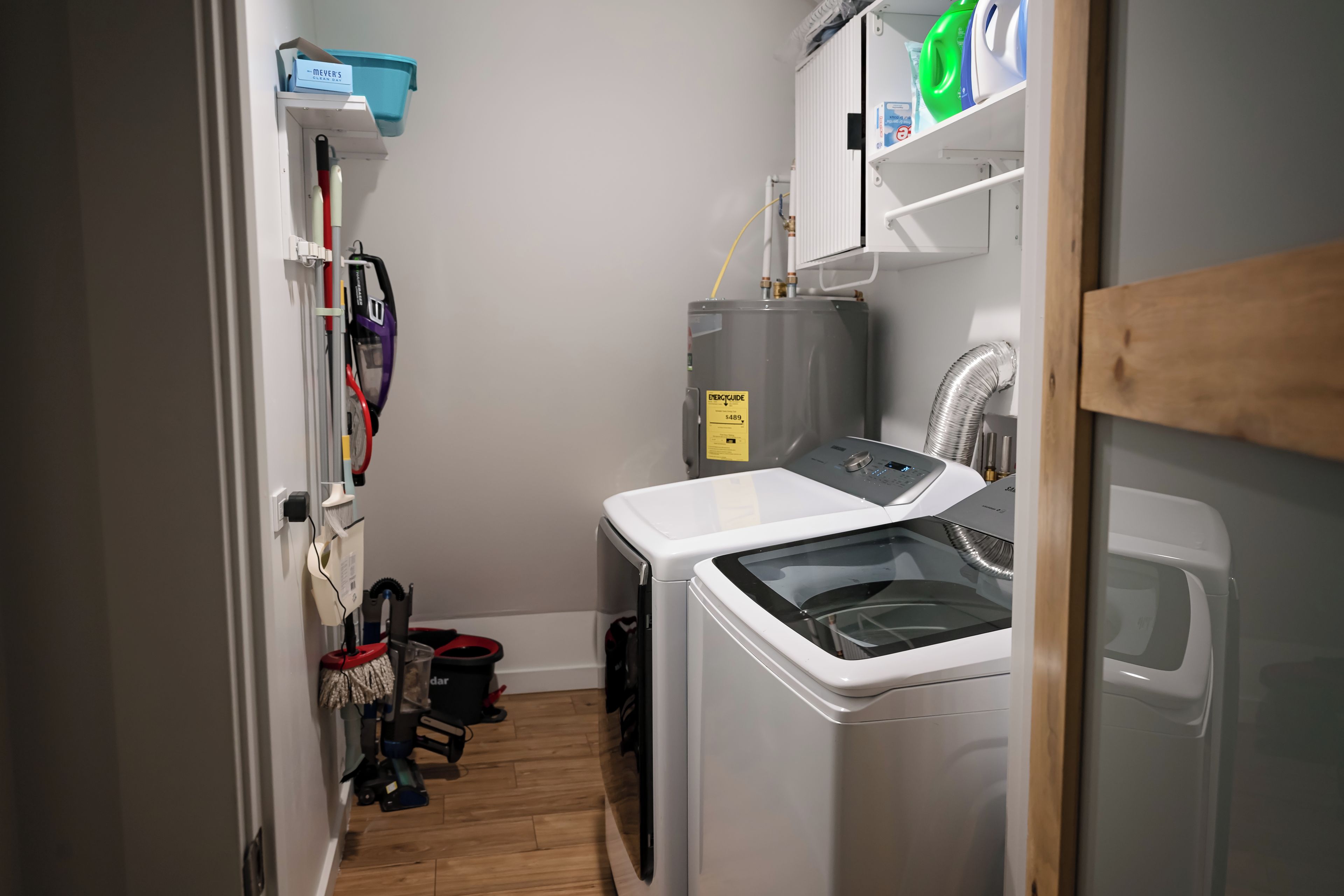 Een wasserette met een voorlader wasmachine en droger, een boiler en een dweil en emmer.