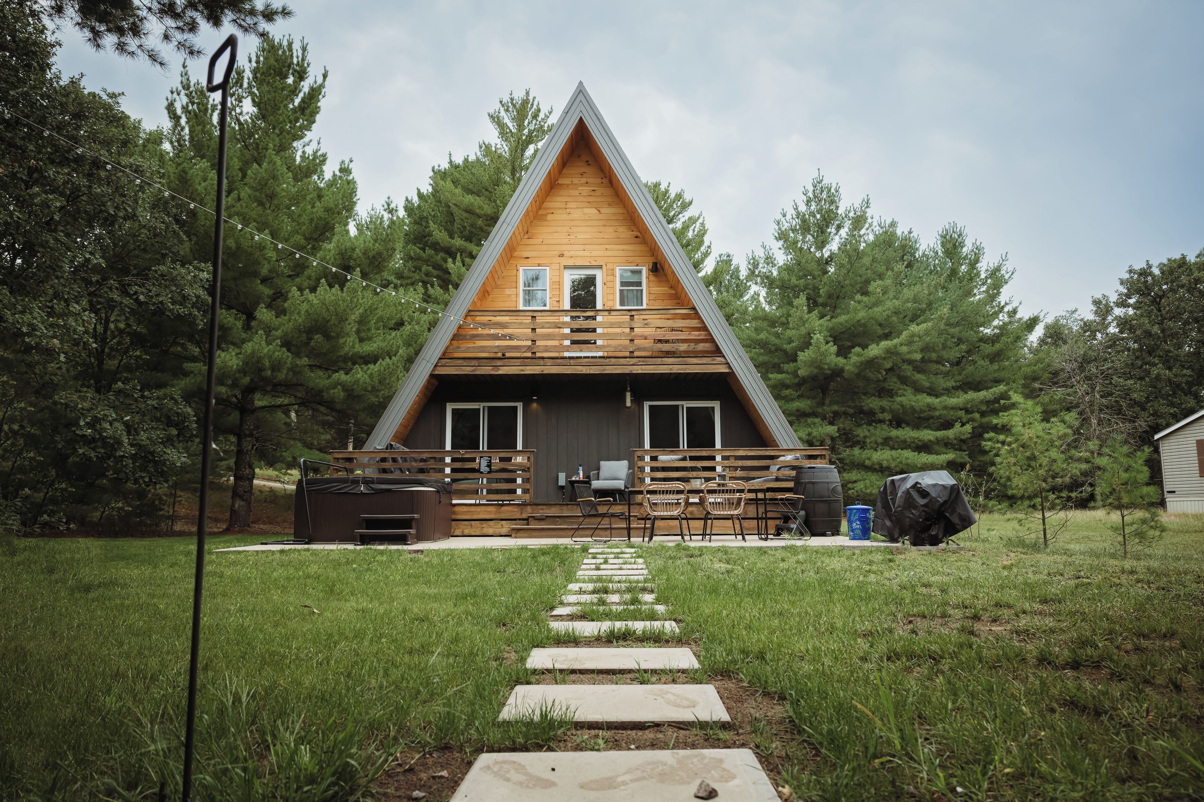 A wooden cabin with a sloped roof, a porch with seating, and a pathway leading to the entrance.