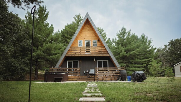 A wooden cabin with a sloped roof, a porch with seating, and a pathway leading to the entrance. - Cozy A-frame w/HOT TUB, 5min walk to lake, King Bed, 30 min to Dells (Friendship)