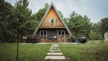 A wooden cabin with a sloped roof, a porch with seating, and a pathway leading to the entrance.