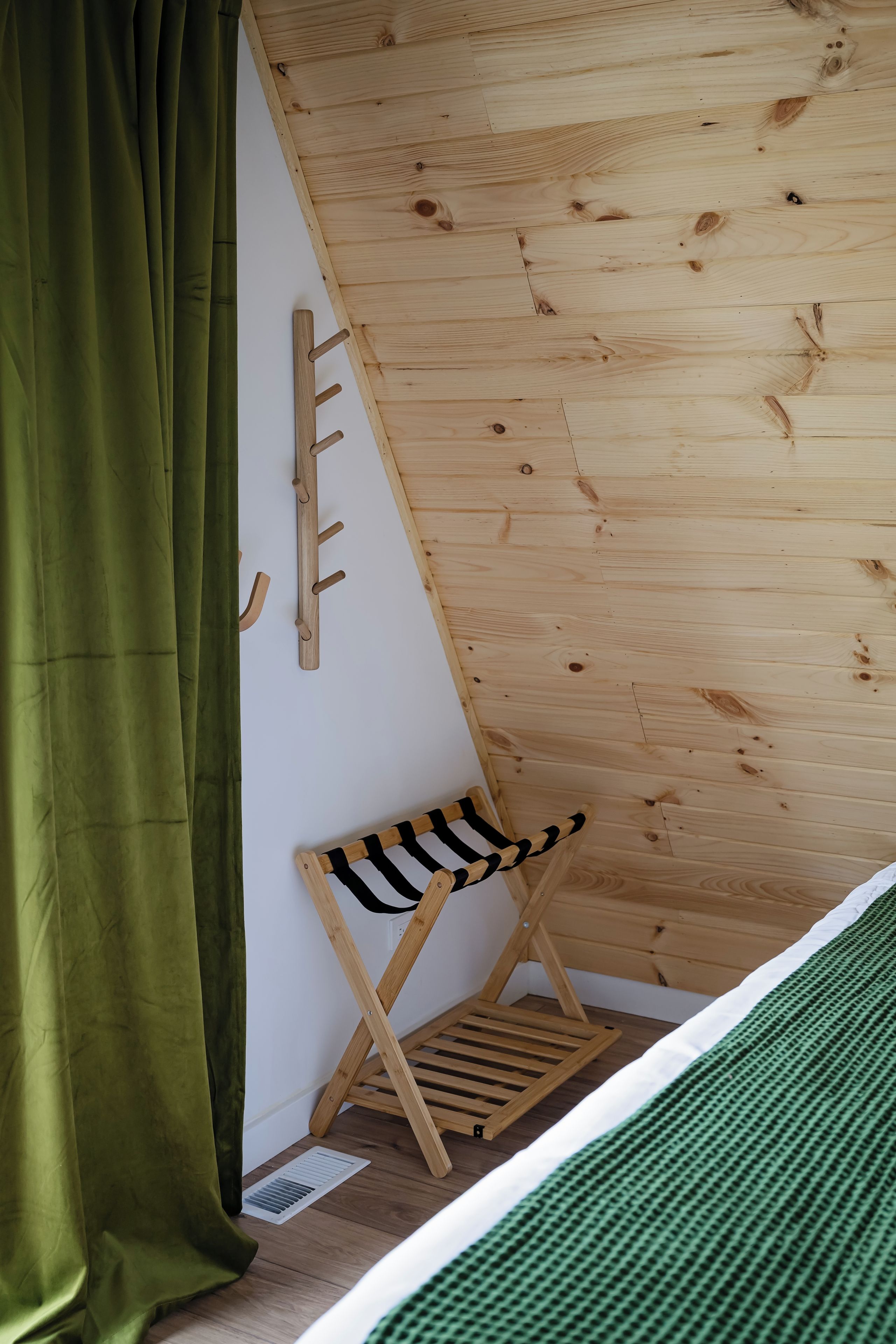 Una habitación con techo inclinado, un banco de madera, un perchero en la pared y una cortina verde.