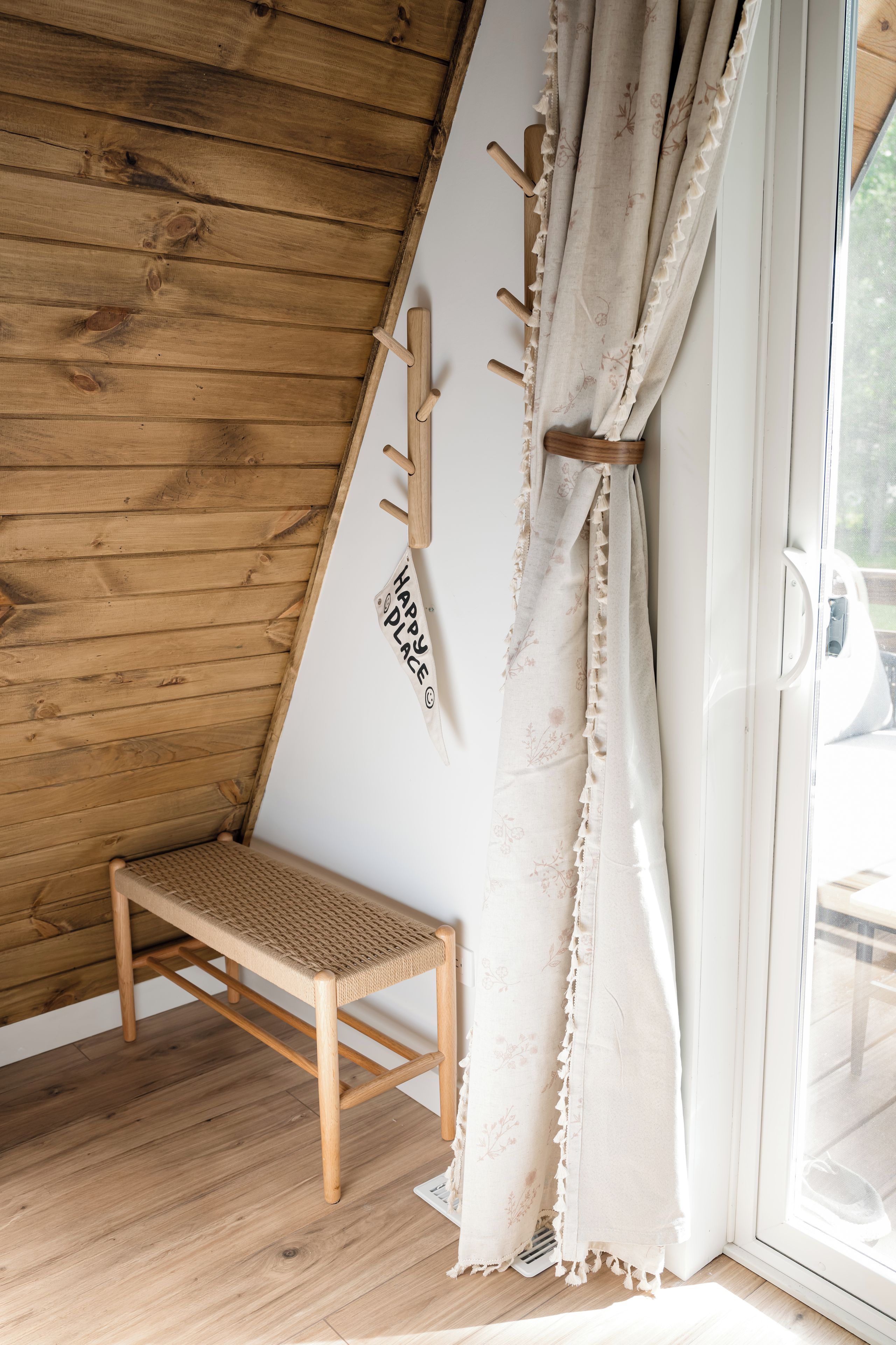 A wooden bench with a woven seat, a wall-mounted coat rack, and a window with a curtain.