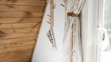 A wooden bench with a woven seat, a wall-mounted coat rack, and a window with a curtain.