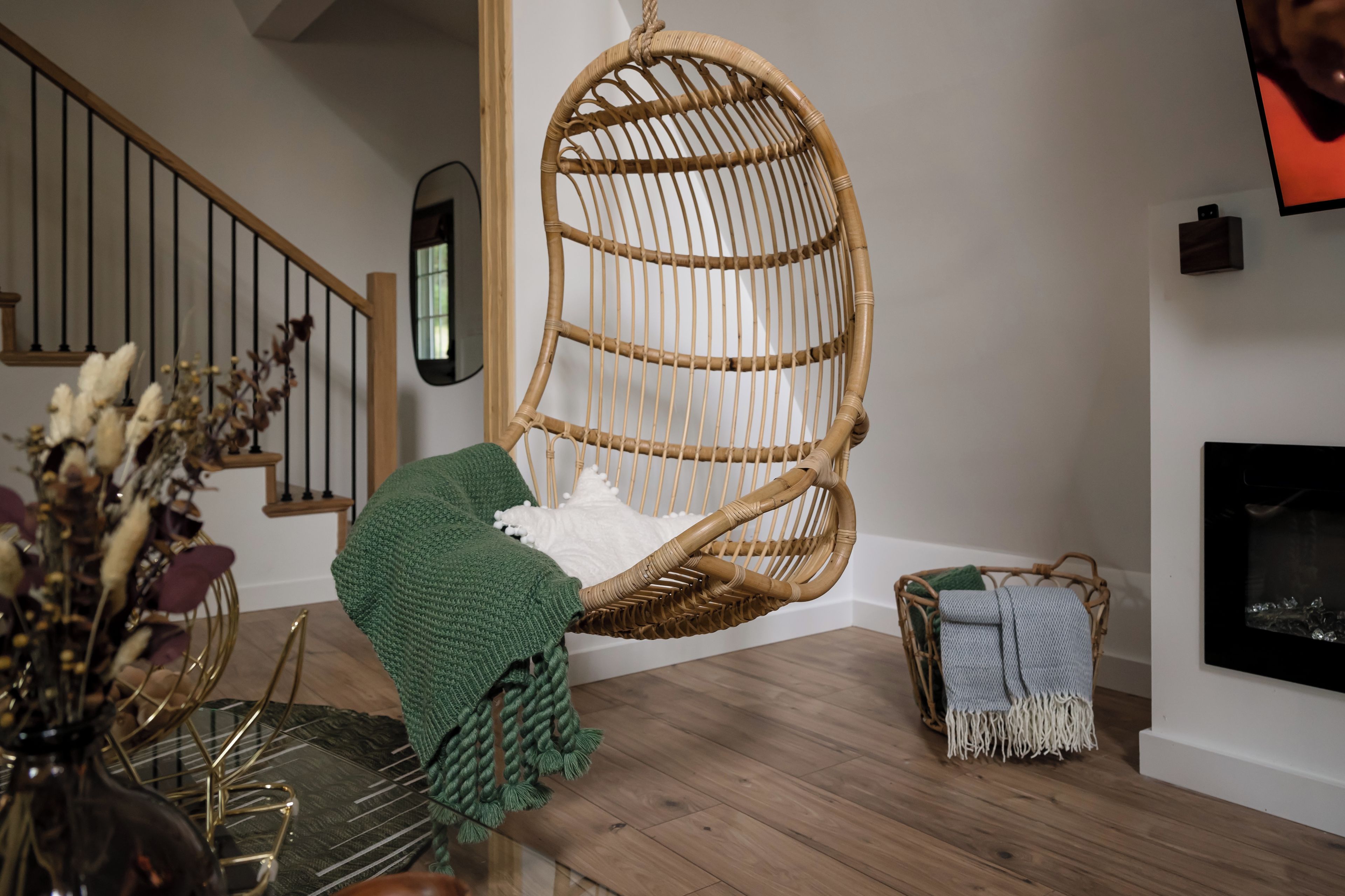 A room with a hanging chair, a fireplace, a staircase, and a dining area with a glass table.