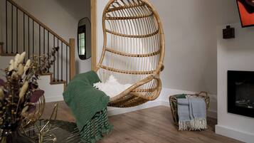 A room with a hanging chair, a fireplace, a staircase, and a dining area with a glass table.
