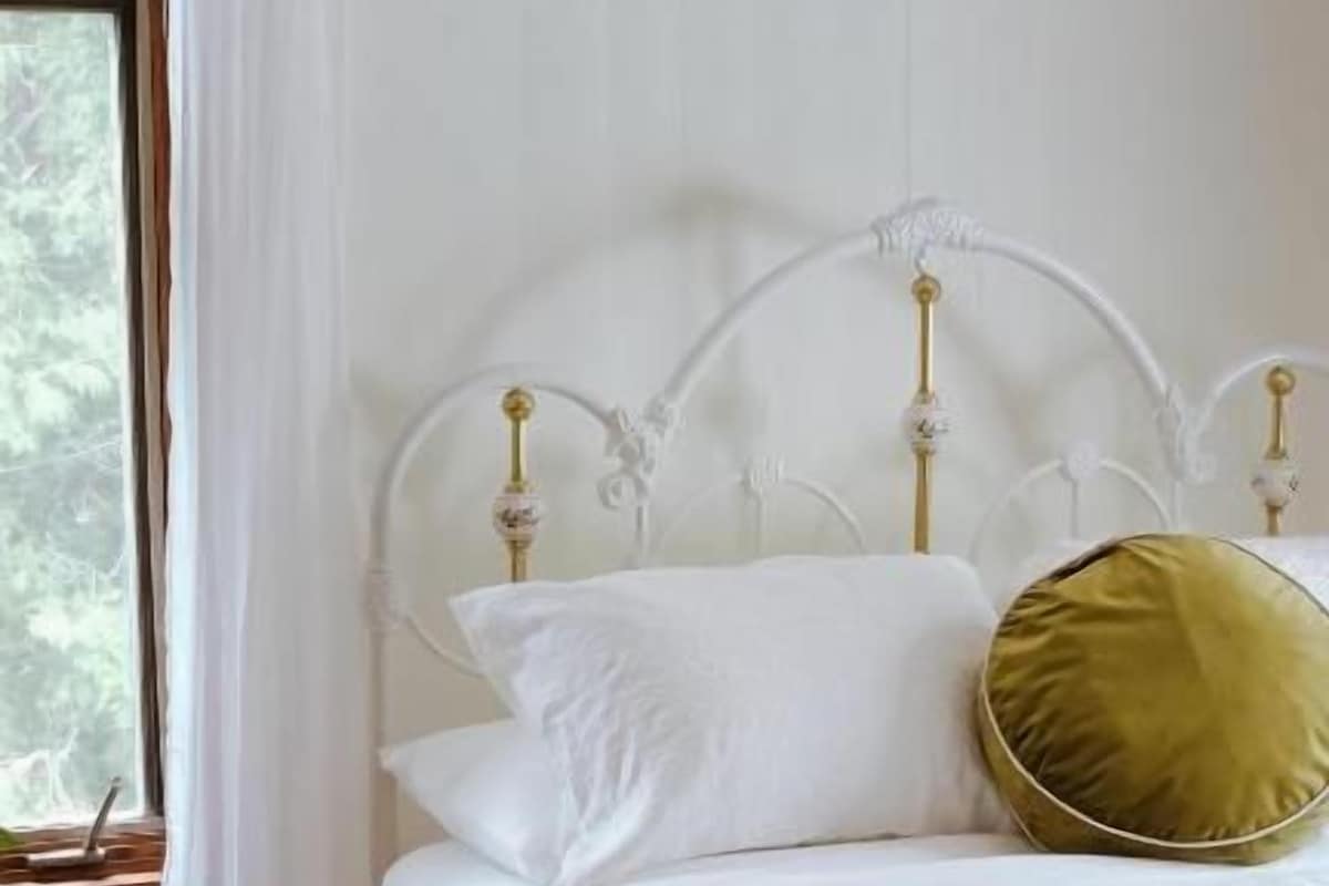 Un letto con una testiera bianca, biancheria da letto bianca e un cuscino verde.