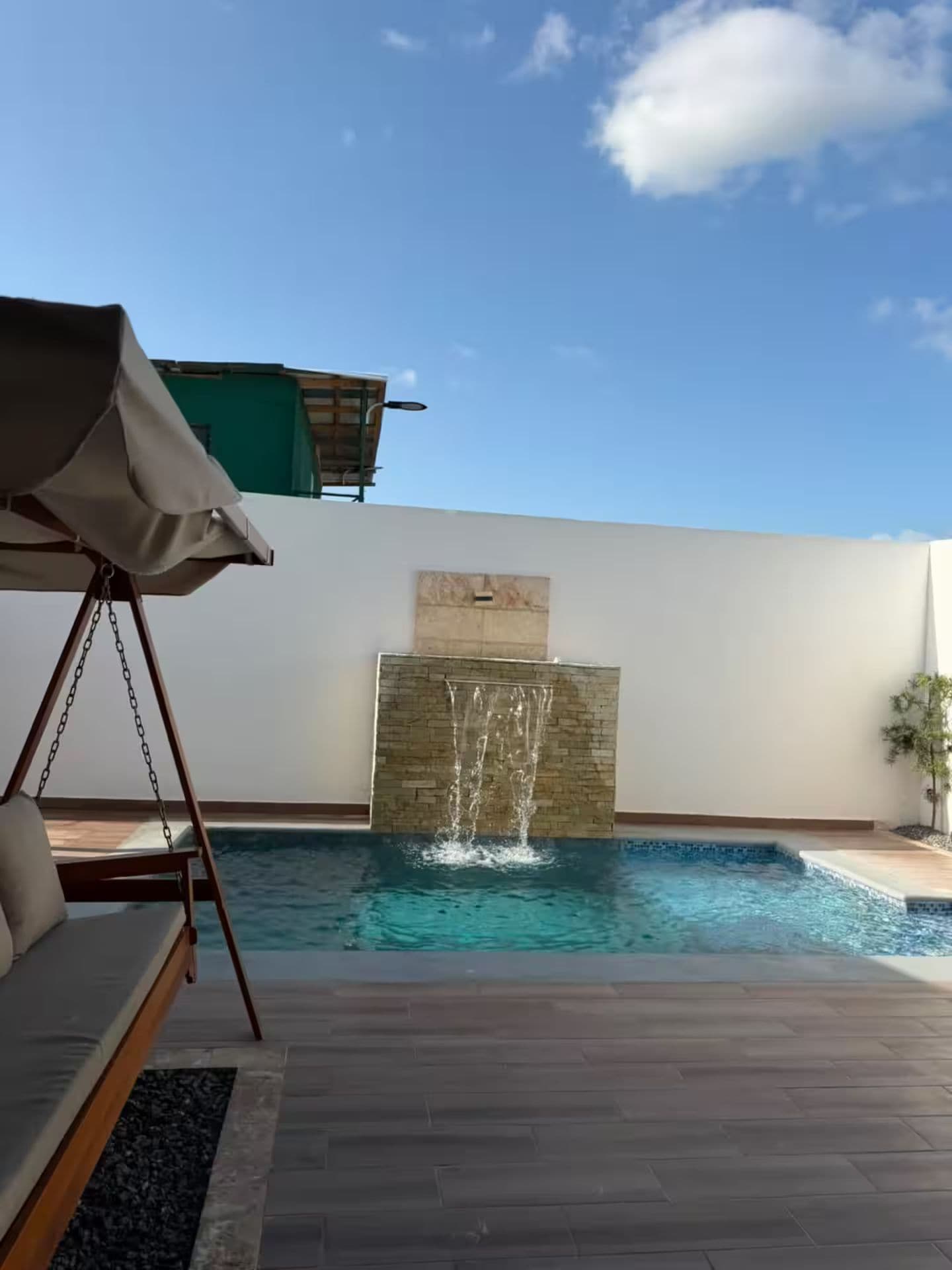 Een zwembad met een waterval, een hangstoel en een overdekte zitruimte.