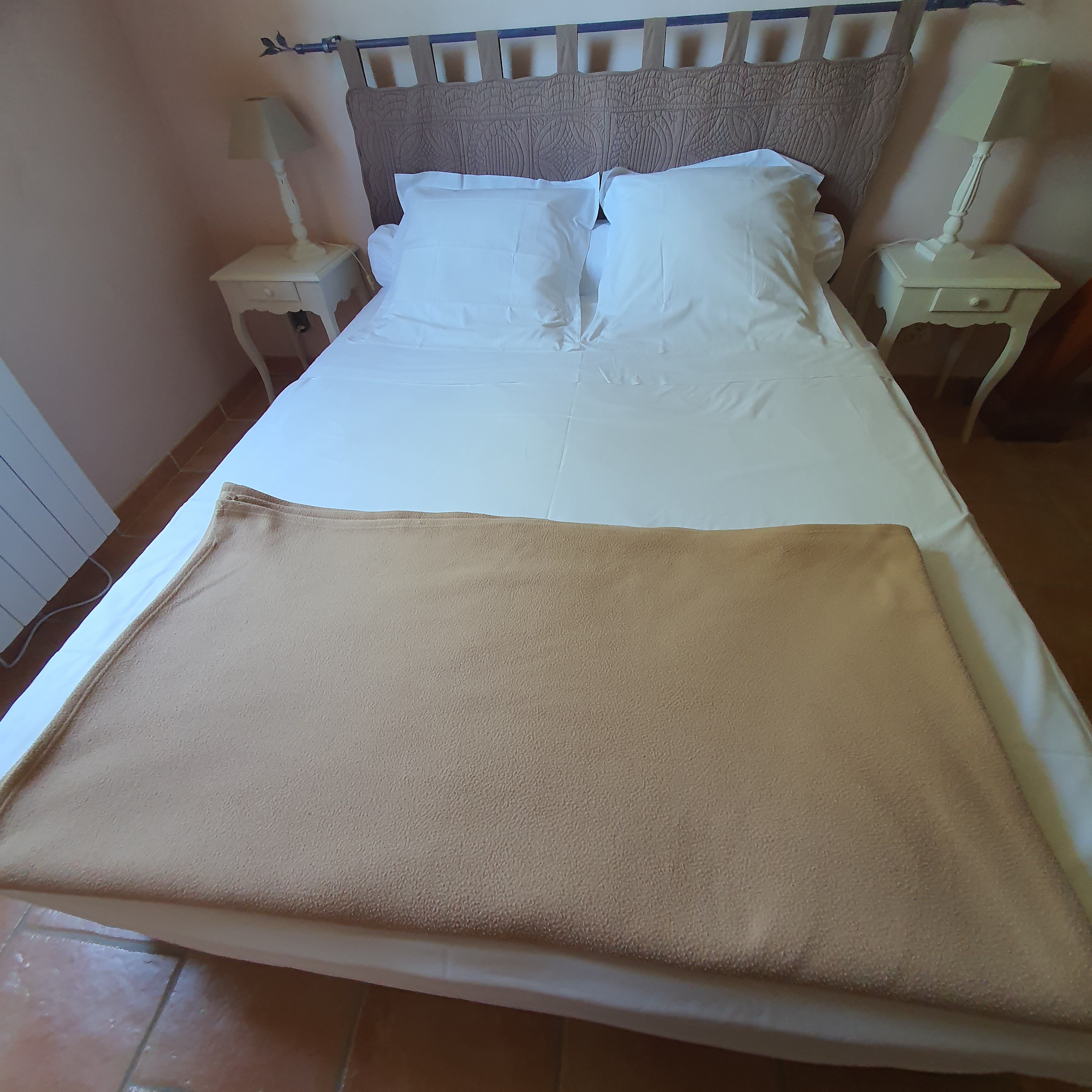 A neatly made bed with white bedding and a brown blanket, flanked by two bedside tables with lamps.