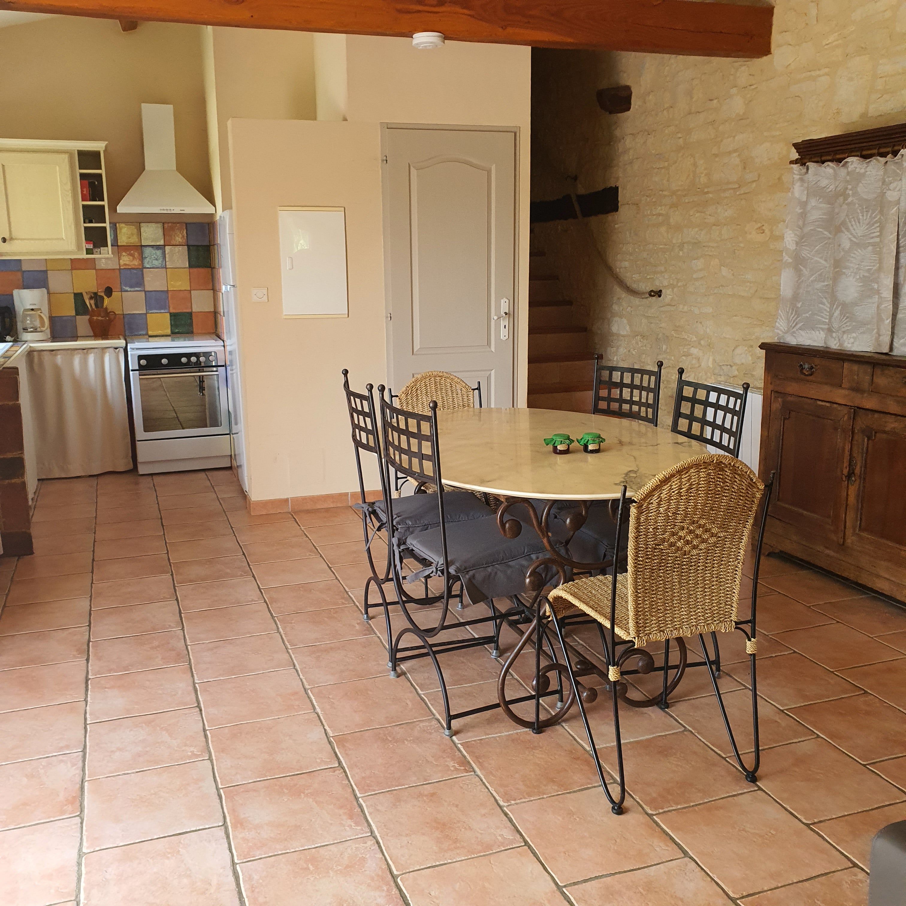 Un coin repas avec une table ronde et des chaises, une cuisine équipée d’un four et un mur en pierre.