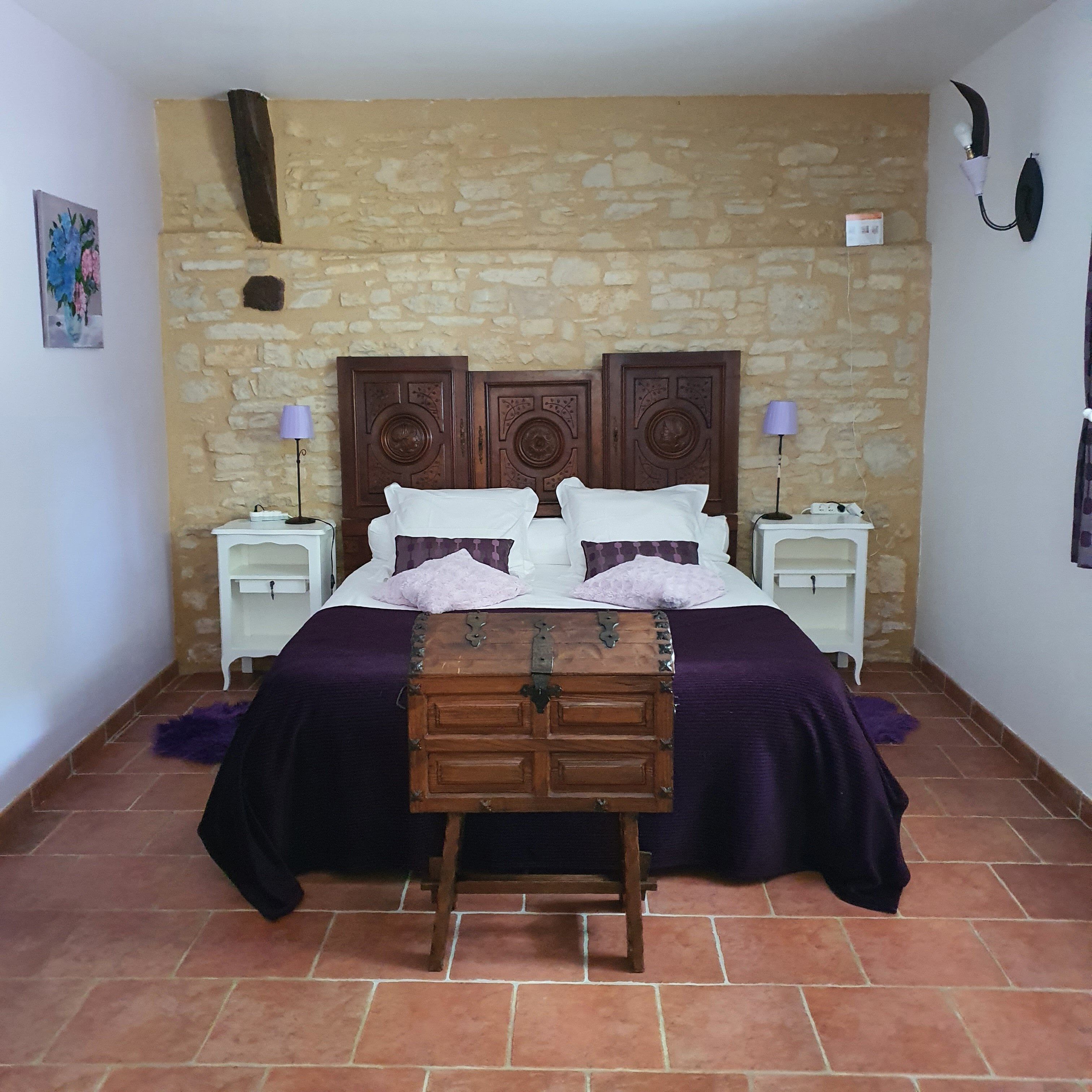 Ein Schlafzimmer mit einer Steinwand, einem hölzernen Bett mit einer Kommode, zwei Nachttischen mit Lampen und einem kleinen Gemälde an der Wand.