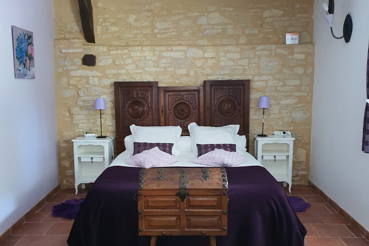 Un dormitorio con pared de piedra, una cama de madera con mesita de noche y una pequeña pintura en la pared.