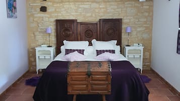 Ein Schlafzimmer mit einer Steinwand, einem hölzernen Bett mit einer Kommode, zwei Nachttischen mit Lampen und einem kleinen Gemälde an der Wand.