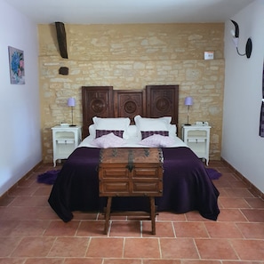 Un dormitorio con pared de piedra, una cama de madera con mesita de noche y una pequeña pintura en la pared.