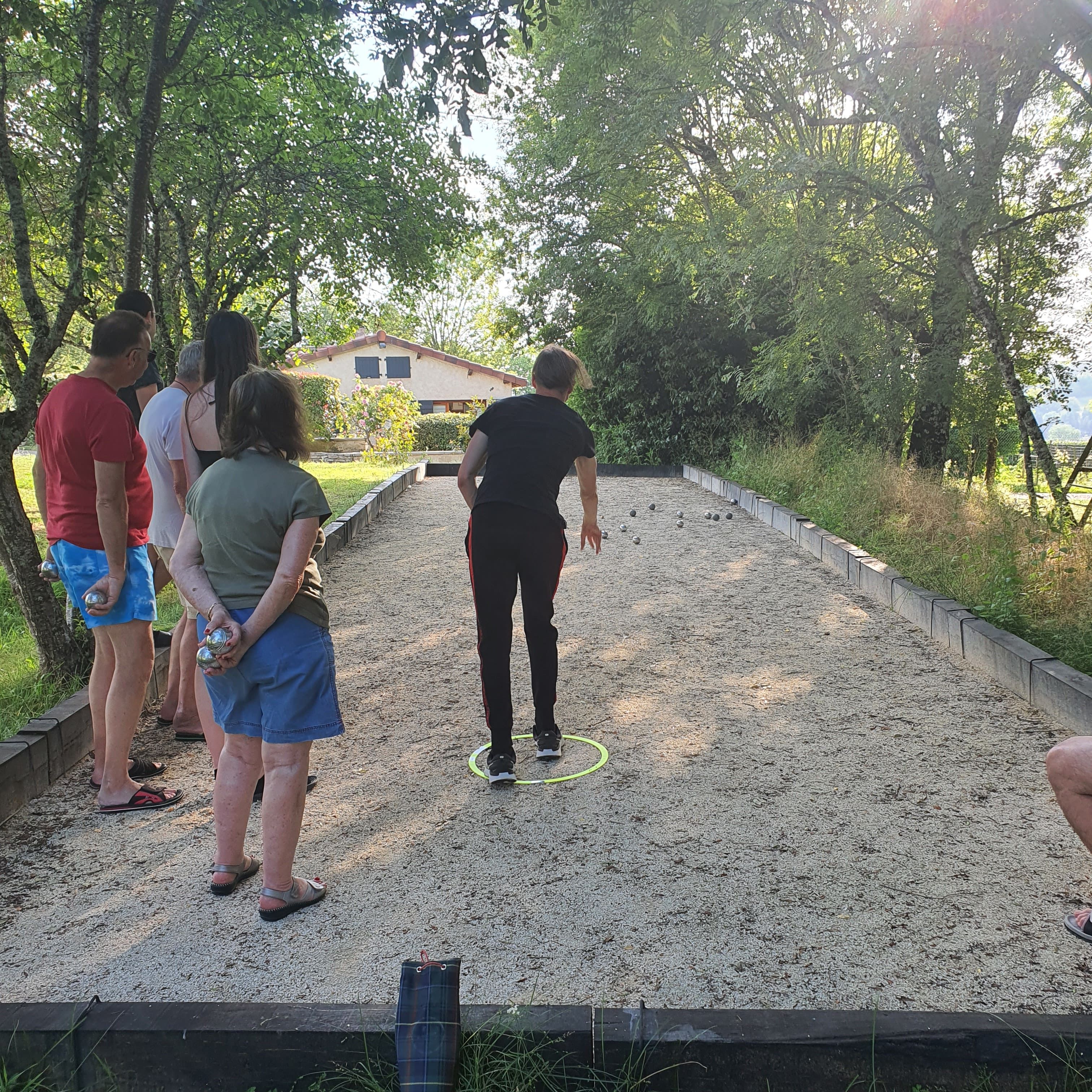 Eine Gruppe von Menschen spielt auf einem Kiesplatz, im Hintergrund ein Haus.